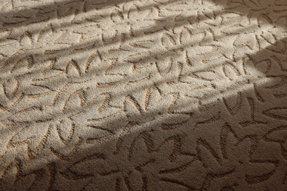 Close-up of a beige carpet with visible handwriting and abstract patterns created by the carpet fibers. The surface appears clean and well-maintained, reflecting light from above, with a slight shadow cast across part of the texture. The carpet is situated in a room with natural lighting, and no other furniture or objects are visible, emphasizing the detailed texture of the fibres. This image illustrates the importance of surface cleaning and deep cleaning in maintaining the hygiene and appearance of domestic carpets, as highlighted by Putney Carpet Cleaners on their page about variations in carpet cleaning quotes.
